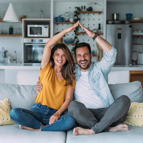 um casal a simular  aforma de um telhado com os braços e mãos sobre as cabeças